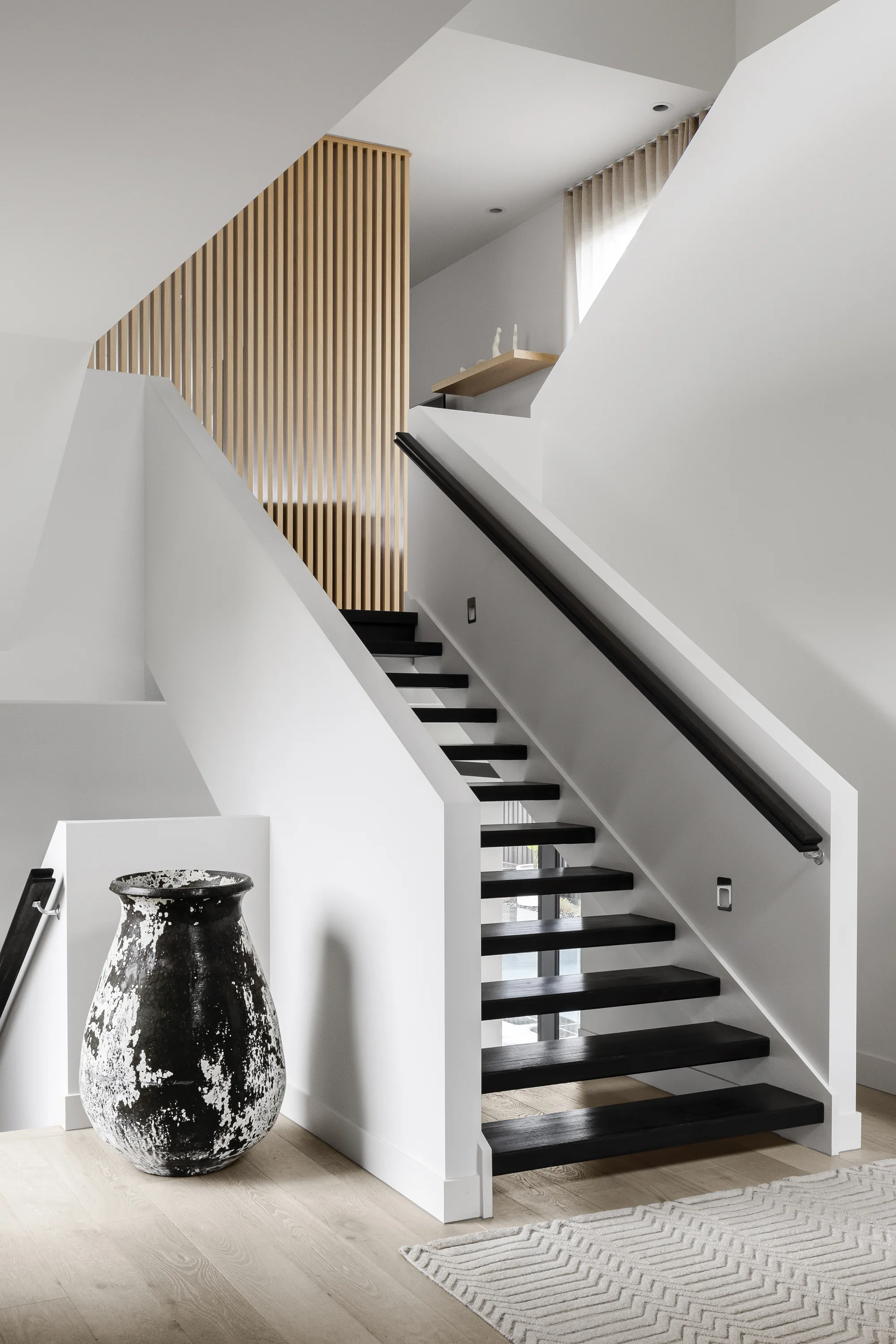 Sculptural staircase with dark treads and a timber batten screen